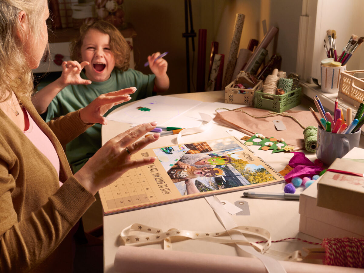 Eine Frau sitzt mit einem Kind an einem Tisch, sie lächeln sich an. Auf dem Tisch liegen ein Kalender sowie Verpackungsmaterial.