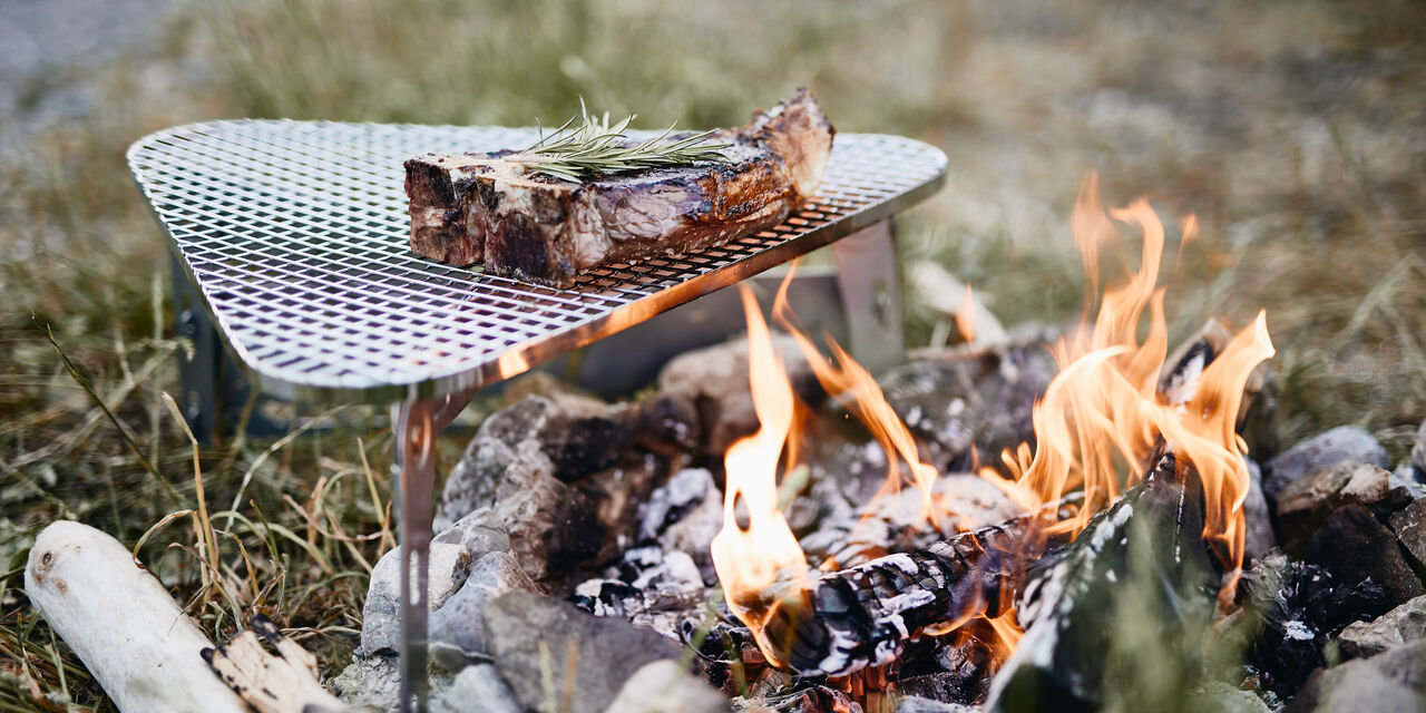 Gleich gar: Über loderndem Lagerfeuer wird ein Stück Fleisch gegrillt.