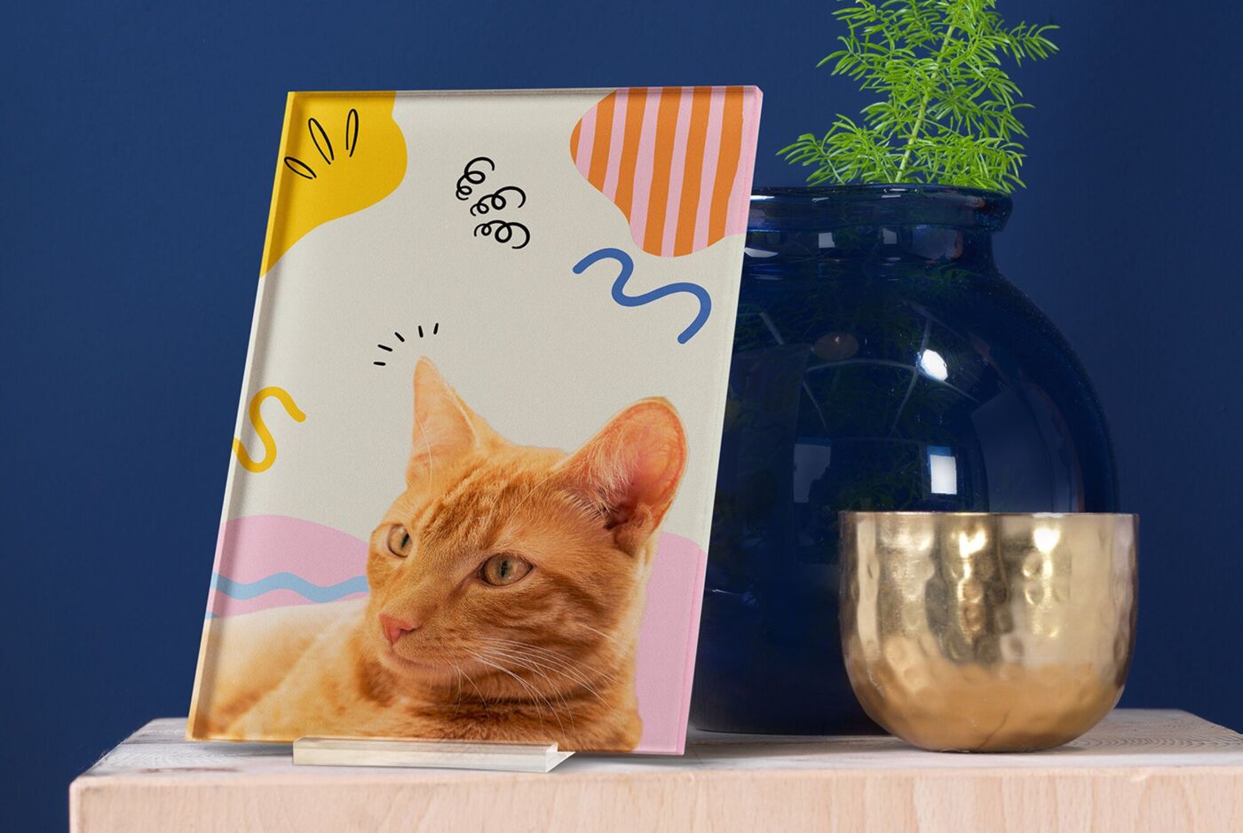 Freigestelltes Foto hinter Acrylglas mit orangefarbener Katze und buntem, grafischem Hintergrund steht auf einem Ständer.