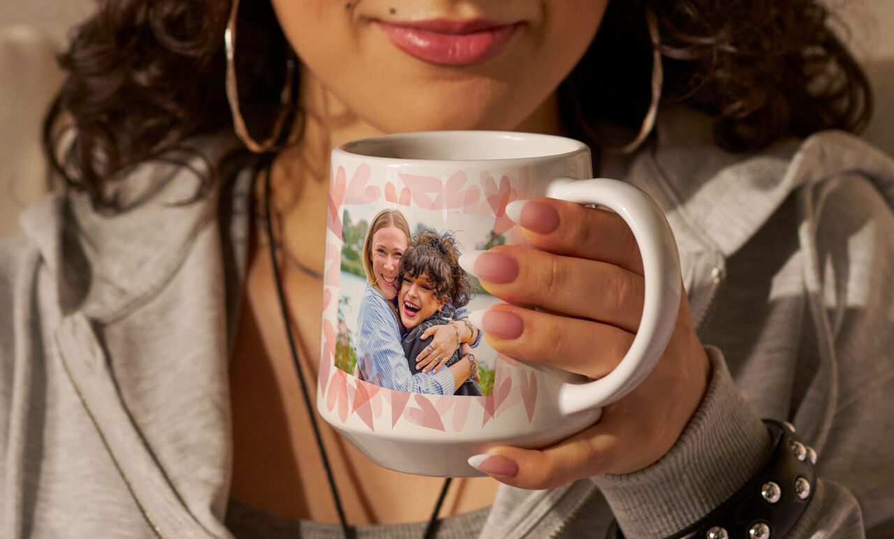 Eine Person hält einen personalisierten Foto-Kaffeebecher mit einem Foto von zwei lächelnden Personen.