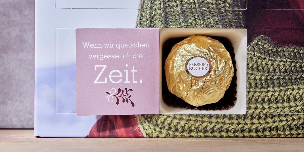 Auf der Innenseite eines geöffneten Türchens stehen die Worte “Wenn wir quatschen, vergesse ich die Zeit”. Darunter befindet sich ein Mistelzwei-Clipart. Hinter dem Adventskalendertürchen steckt eine Kugel Ferrero Rocher.