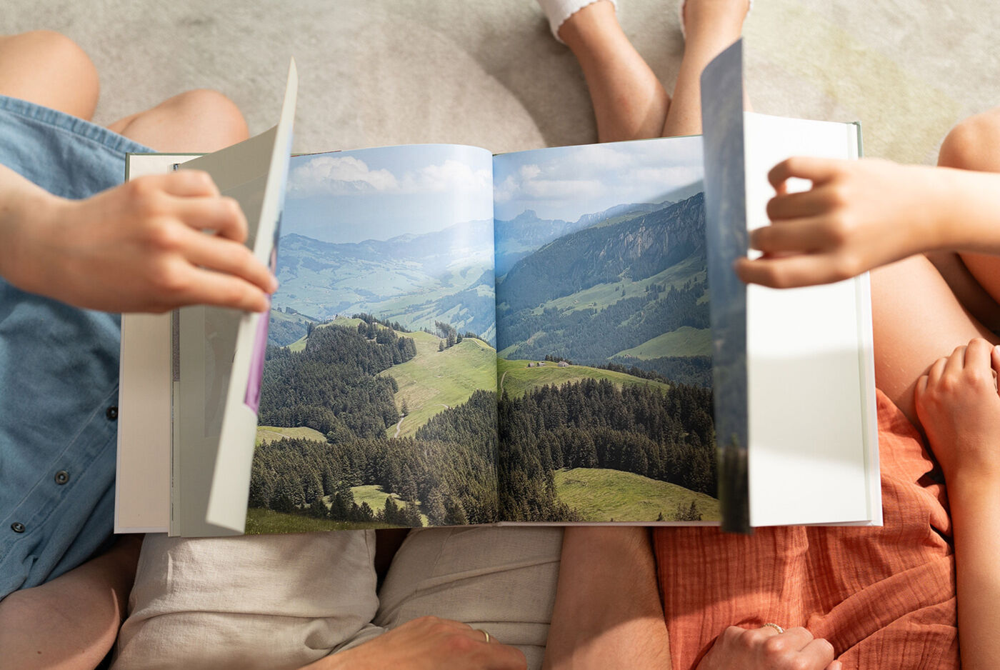 Menschen öffnen eine Panoramaseite im CEWE FOTOBUCH mit Berglandschaft